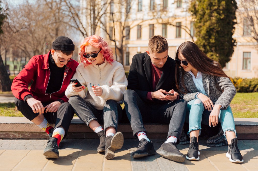 front-view-four-friends-together-outdoors-checking-their-smartphones